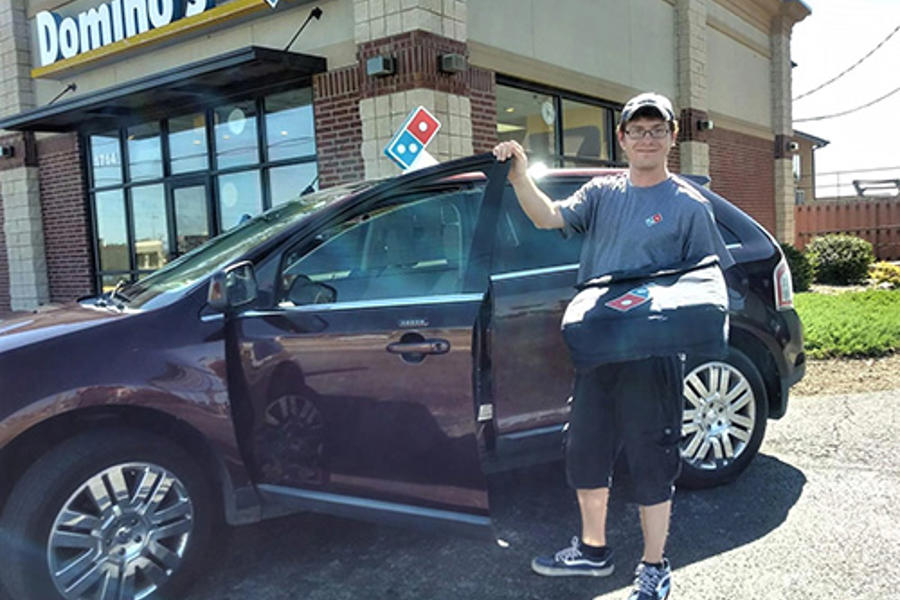 Un hombre sosteniendo una bolsa y de pie junto a un coche