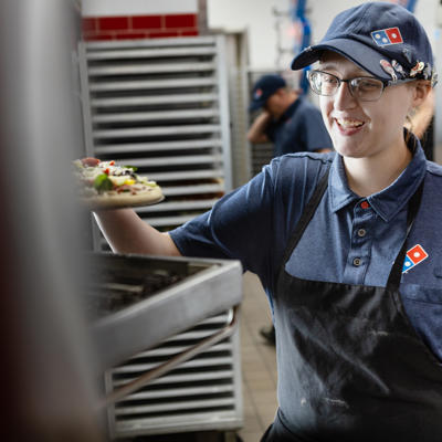 a woman wearing a blue hat and apron holding a pizza