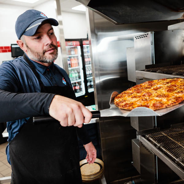 a man in a blue hat holding a pizza in a large oven